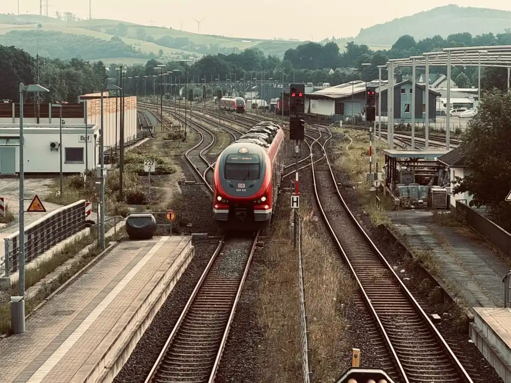 Eisenbahnstrecke mit einem roten Regionalzug und Bahnhof